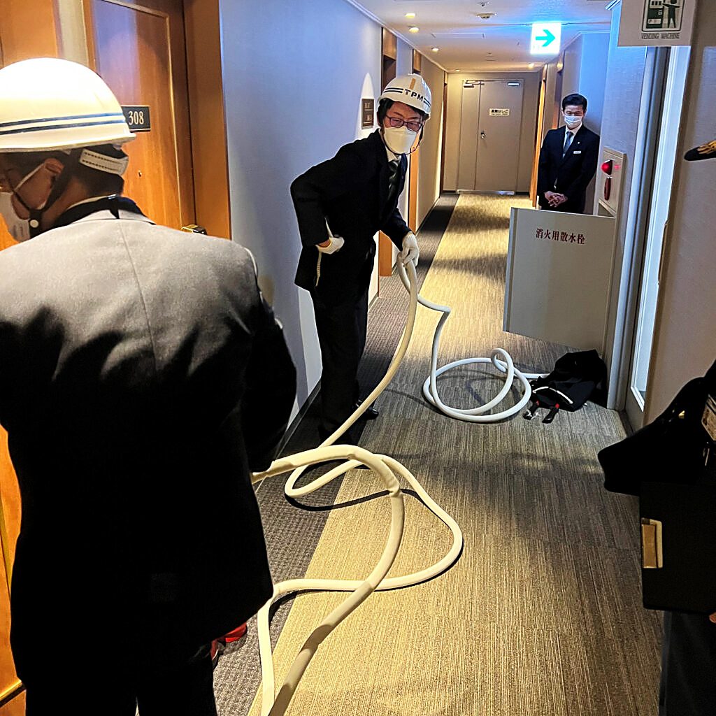 消火用散水栓のホースを伸ばして点検するホテルスタッフ